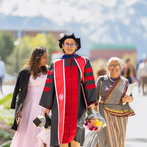 new grad walking on campus in front of two family members